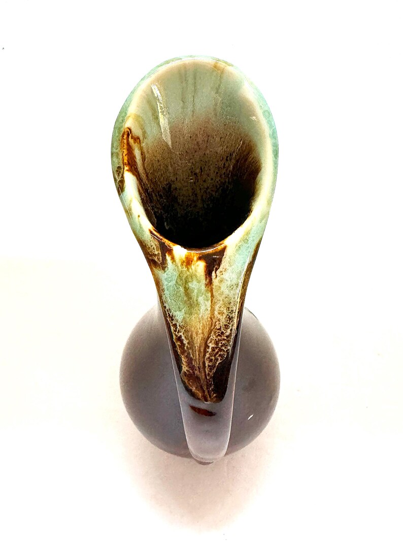 May include: A brown and green ceramic vase with a unique, curved spout. The vase has a mottled glaze with brown, green, and white accents.