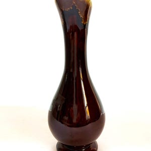 May include: A brown ceramic vase with a flared opening and a rounded base. The vase has a glossy finish and a subtle marbled pattern.