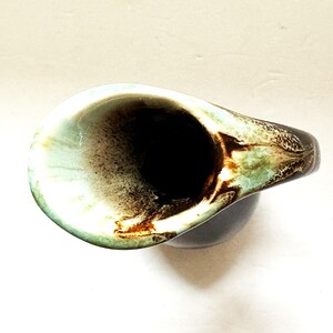 May include: A brown and green ceramic pitcher with a wide, rounded spout. The pitcher has a mottled glaze with brown, green, and white swirls.