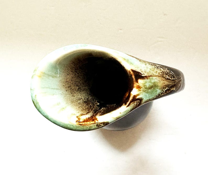 May include: A brown and green ceramic pitcher with a wide, rounded spout. The pitcher has a mottled glaze with brown, green, and white swirls.