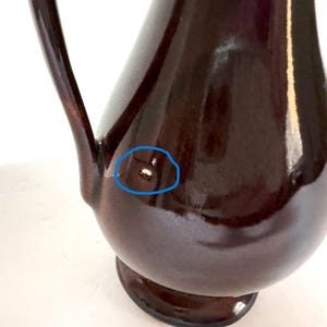 May include: A dark brown ceramic pitcher with a wide base and a handle. The pitcher has a small imperfection on the side.