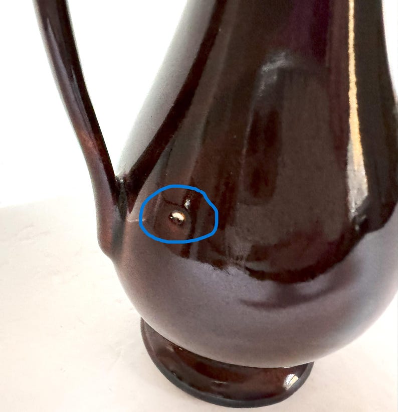 May include: A dark brown ceramic pitcher with a wide base and a handle. The pitcher has a small imperfection on the side.