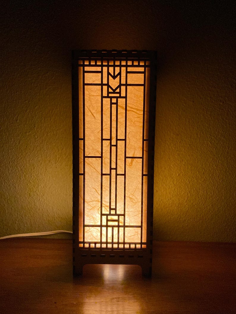 May include: A wooden table lamp with a geometric design and a warm, yellow light emanating from the lampshade.