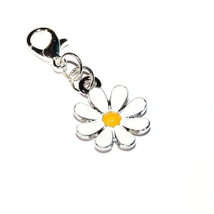 Könnte beinhalten: Ein Gänseblümchen-Anhänger mit weißen Blütenblättern und einem gelben Zentrum, befestigt an einem silberfarbenen Karabinerverschluss. Der Anhänger ist ein floraler Schmuck, ideal für ein Armband oder eine Halskette.