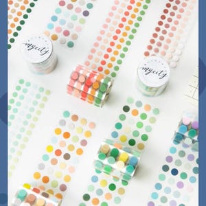 May include: An overhead shot displays rolls of colorful dot washi tape and strips of dot stickers. The tape rolls have the text "mycity" on them. The dots are in various colors, including green, orange, pink, and blue.