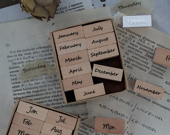 May include: Wooden stamps with months of the year and days of the week. The stamps are in a wooden box and scattered on a vintage paper background. The stamps are in a variety of fonts.