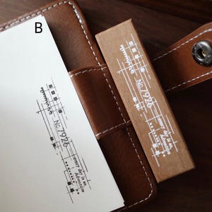 May include: A rectangular wooden rubber stamp with white printed text and graphics including the label No.7926 and the phrase every day is an Adventure. The stamp is positioned next to a white paper showing a black ink impression of the same design.