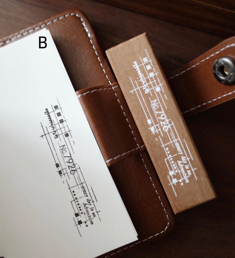 May include: A rectangular wooden rubber stamp with white printed text and graphics including the label No.7926 and the phrase every day is an Adventure. The stamp is positioned next to a white paper showing a black ink impression of the same design.