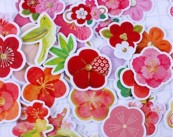 May include: A collection of colorful floral stickers in various shapes and sizes. The stickers feature red, pink, and orange flowers, along with green leaves and a yellow bird. Some flowers have gold accents. The stickers are arranged on a white background.