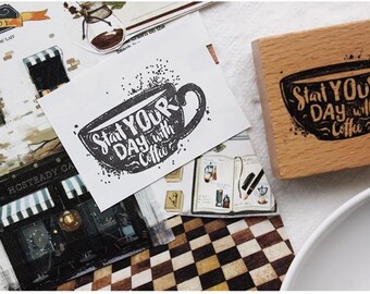 May include: A collection of coffee-themed stationery items. A stamp with the text "Start Your Day with Coffee" is next to a printed image of a coffee cup with the same text. Other items include a cafe illustration and a notebook.