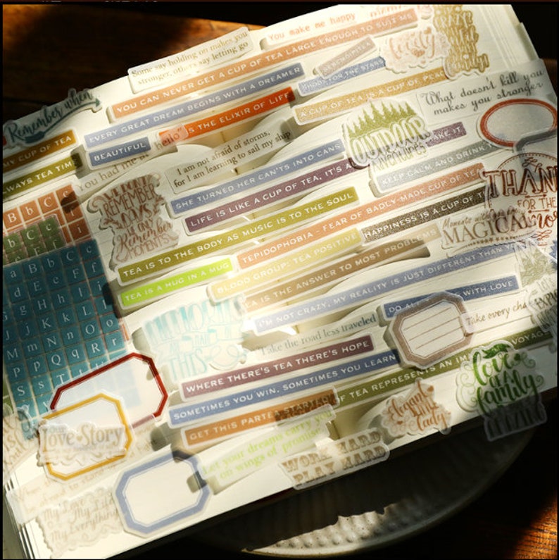 May include: A collection of colorful, patterned stickers with various quotes and sayings. The stickers are mostly rectangular and feature a variety of fonts and designs. Some of the quotes include "Remember when", "Every great dream begins with a dreamer", "Life is like a cup of tea, it's all", "Tea is to the body as music is to the soul", "Where there's tea there's hope", and "Love is a family".
