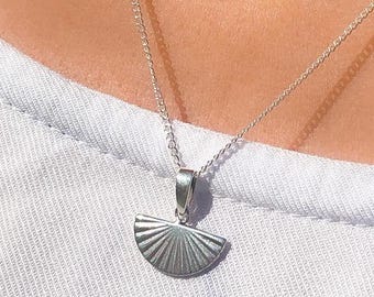 May include: A silver necklace with a delicate fan-shaped pendant. The pendant has a textured, sunburst design.
