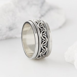 May include: A silver spinning ring with a detailed, intricate design. The ring is made of sterling silver and has a smooth, polished finish.