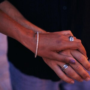 May include: Two hands with a silver ring on one finger and a silver bracelet on one wrist.