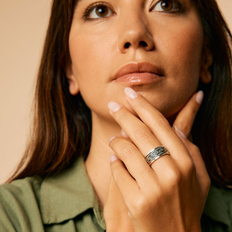 May include: A silver ring with a detailed, intricate design. The ring is worn on the finger of a person with light skin.