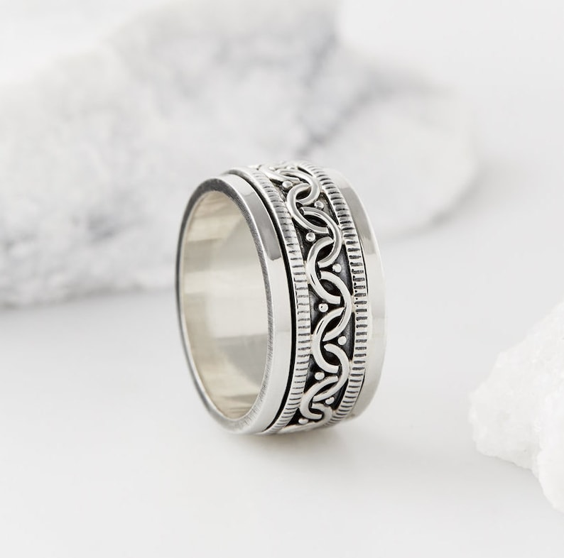 May include: A silver spinning ring with a detailed, intricate design. The ring is made of sterling silver and has a smooth, polished finish.