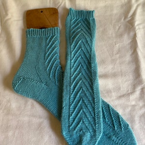 Puede incluir: Un par de calcetines azules de punto con un patrón de chevron. Los calcetines están colocados sobre una superficie blanca.