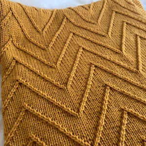 May include: A mustard yellow knitted throw blanket with a chevron pattern.