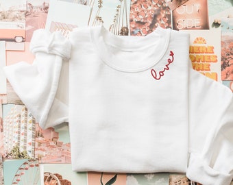 May include: White sweatshirt with long sleeves and a red embroidered word "love" on the front.