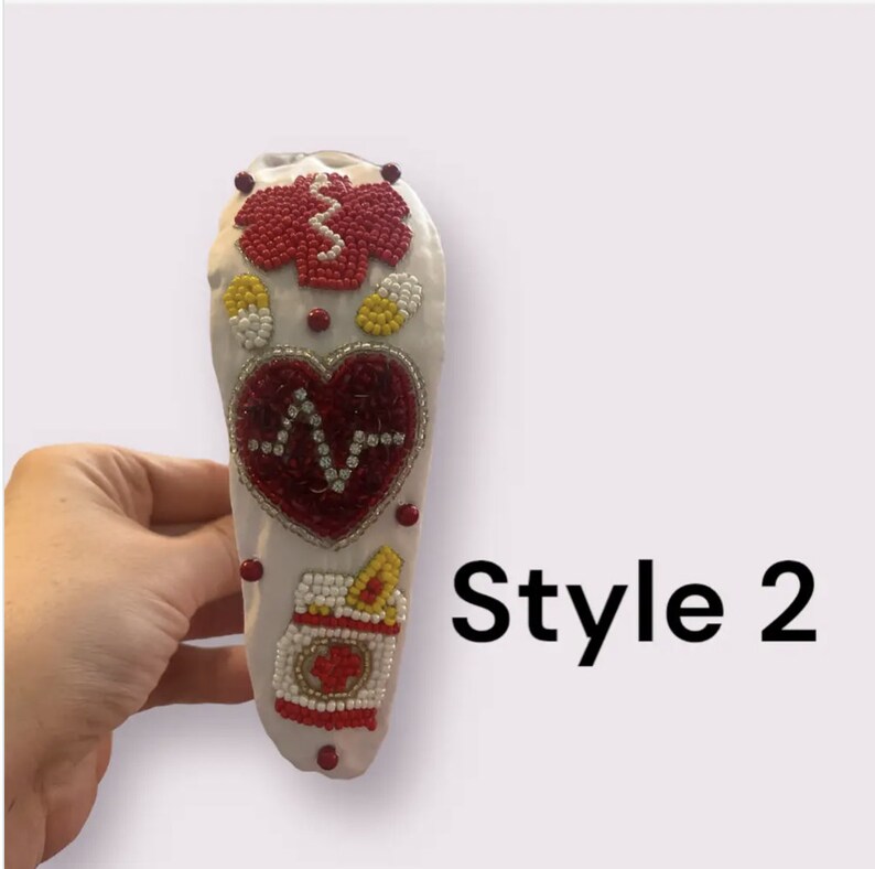 May include: White headband with red, yellow, and white beaded designs. The designs include a heart with a heartbeat symbol, a pill bottle, and a medical symbol. The headband is labeled "Style 2".