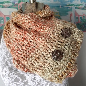 May include: A crocheted cowl in shades of beige, peach, and brown with two decorative metal buttons.