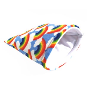 May include: A blue fleece pet bed with a rainbow and cloud pattern. The bed has a white fleece lining.