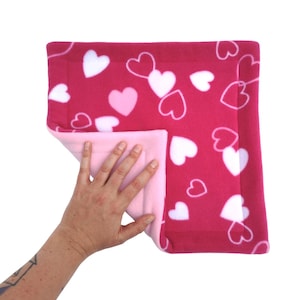 May include: A pink and white fleece pet bed with a heart pattern. The bed is reversible, with a pink side and a white side with pink hearts.