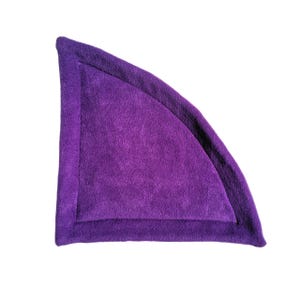 May include: Purple fleece cat bed shaped like a wedge with a rounded edge. The bed has a dark purple border.