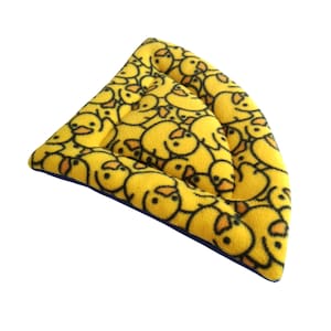 May include: A triangular-shaped pet bed or mat made of soft yellow fleece fabric featuring an all-over pattern of small, cartoon-style yellow ducks with orange beaks. The edges are finished with a dark blue trim, providing a clear contrast.