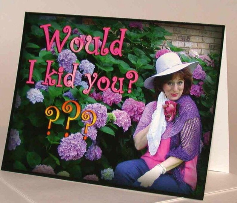 May include: A greeting card with the text "Would I kid you?" in pink letters and question marks. The card features a woman wearing a hat and a purple shawl, set against a backdrop of hydrangeas.