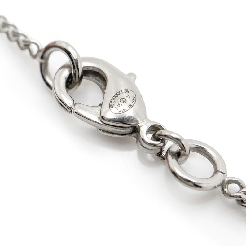 May include: Close-up of a silver-toned necklace clasp with a chain. The clasp is engraved with the brand name and "Made in Italy". The chain and clasp are highly reflective and appear to be made of metal.