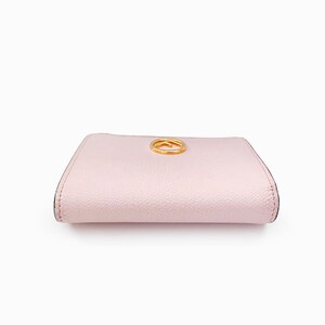 May include: A pale pink leather wallet with a gold-toned logo on the front.
