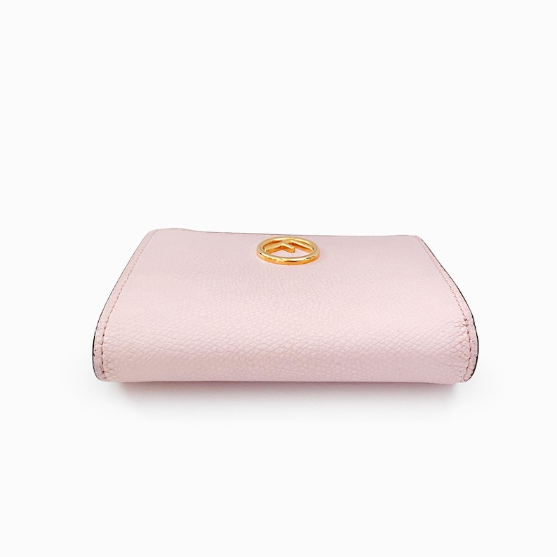 May include: A pale pink leather wallet with a gold-toned logo on the front.