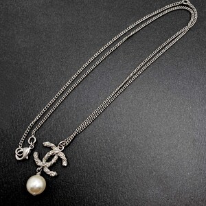 May include: Silver-toned necklace featuring a double-C pendant with a pearl drop. The chain is delicate, and the pendant has a textured design. The necklace is displayed against a dark background.