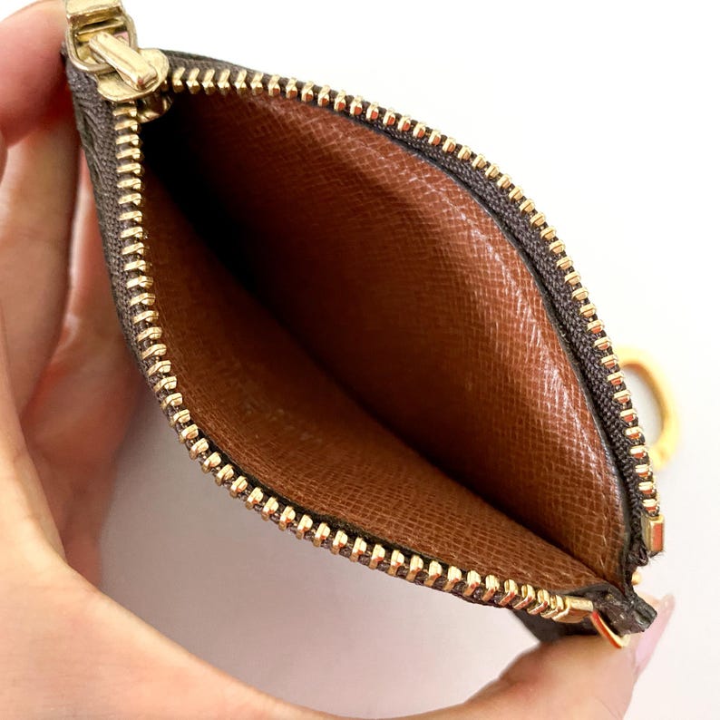 May include: Open brown and tan cardholder with a gold zipper and pull. The interior is a lighter brown with a textured pattern. The zipper is gold-toned, and the cardholder has a small gold ring attached.