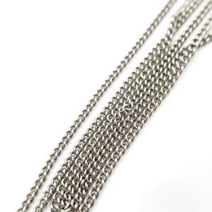 May include: Close-up of several silver-colored chain necklaces against a white background. The chains vary in thickness and are arranged diagonally, showcasing their individual links and textures. The chains are likely for jewelry making.