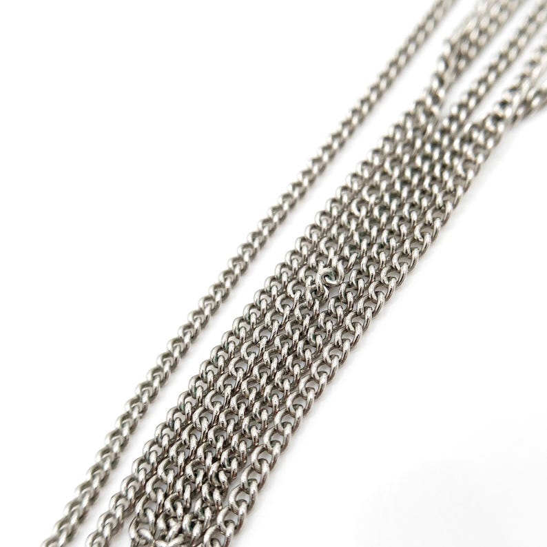May include: Close-up of several silver-colored chain necklaces against a white background. The chains vary in thickness and are arranged diagonally, showcasing their individual links and textures. The chains are likely for jewelry making.