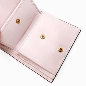 May include: The inside of a pink leather wallet with three gold snaps. The wallet is folded in half and the inside is visible.