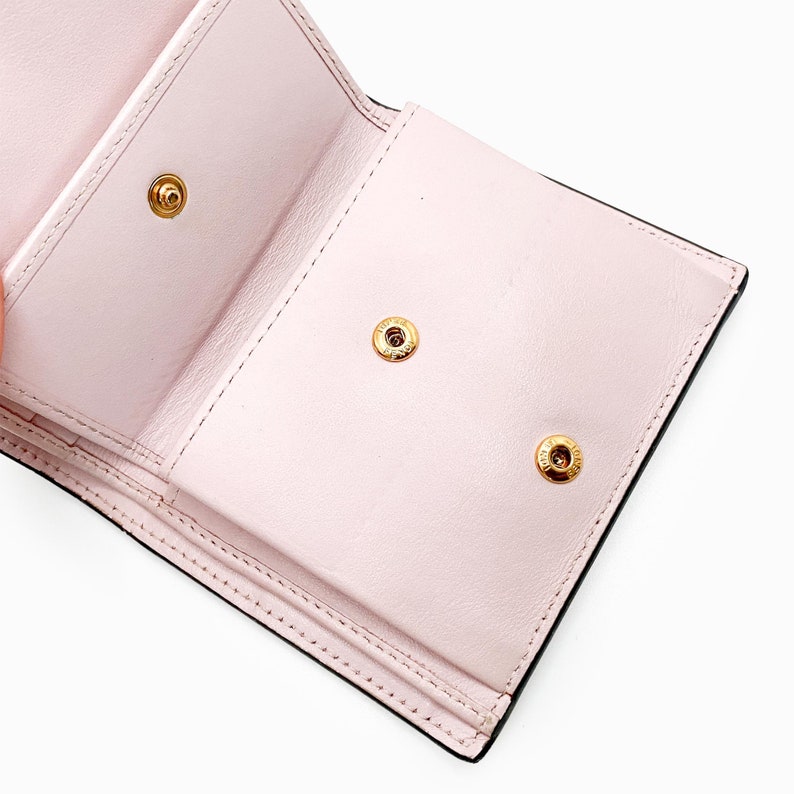May include: The inside of a pink leather wallet with three gold snaps. The wallet is folded in half and the inside is visible.