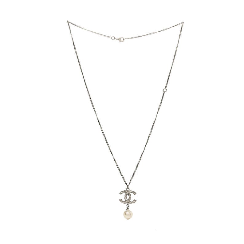 May include: Silver-toned necklace featuring a pendant with a double-C design encrusted with small, clear crystals. A single, round, white pearl dangles below the pendant. The necklace has a delicate chain and a clasp closure.