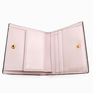 May include: A black leather wallet with a pink interior. The wallet has multiple card slots and a billfold. The wallet is open and the interior is visible. The wallet has a gold Fendi logo on the interior.