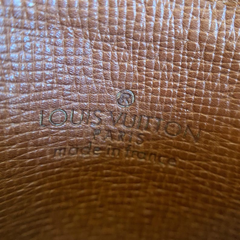 May include: Close-up of a brown leather surface with the embossed text "LOUIS VUITTON PARIS made in france". The leather has a textured pattern and a small circular logo.