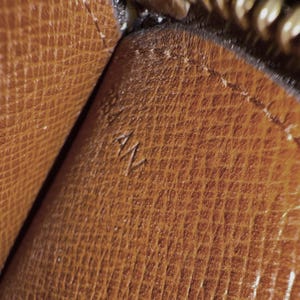 May include: Close-up of a brown leather surface with a textured pattern. The letters "AN" are embossed on the leather. The image shows a portion of a larger item, possibly a wallet or handbag.