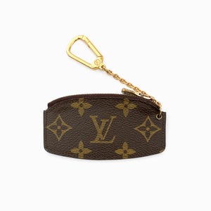 May include: Brown coin purse with a gold-colored chain and clasp. The purse features a repeating pattern of brown floral shapes and the letter "V" in a lighter brown color.