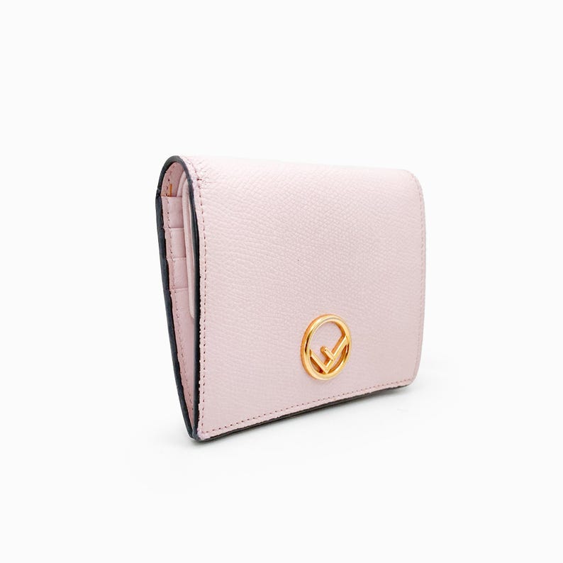 May include: A pale pink leather wallet with a gold Fendi logo. The wallet has a fold-over closure and a small pocket on the front.