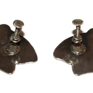 May include: A pair of silver tone clip-on earrings with a unique abstract design. The earrings are made of metal and have a screw-on back.