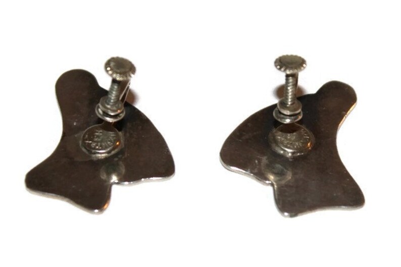 May include: A pair of silver tone clip-on earrings with a unique abstract design. The earrings are made of metal and have a screw-on back.