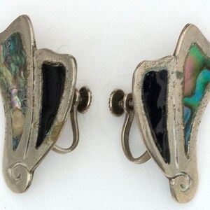 May include: A pair of silver clip-on earrings with black and iridescent abalone shell inlay. The earrings are shaped like a stylized leaf with a curved design at the bottom.