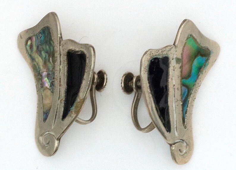 May include: A pair of silver clip-on earrings with black and iridescent abalone shell inlay. The earrings are shaped like a stylized leaf with a curved design at the bottom.