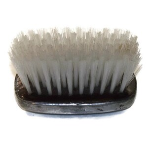May include: A black oval-shaped brush with white bristles. The brush is made of wood and has a smooth, polished finish.